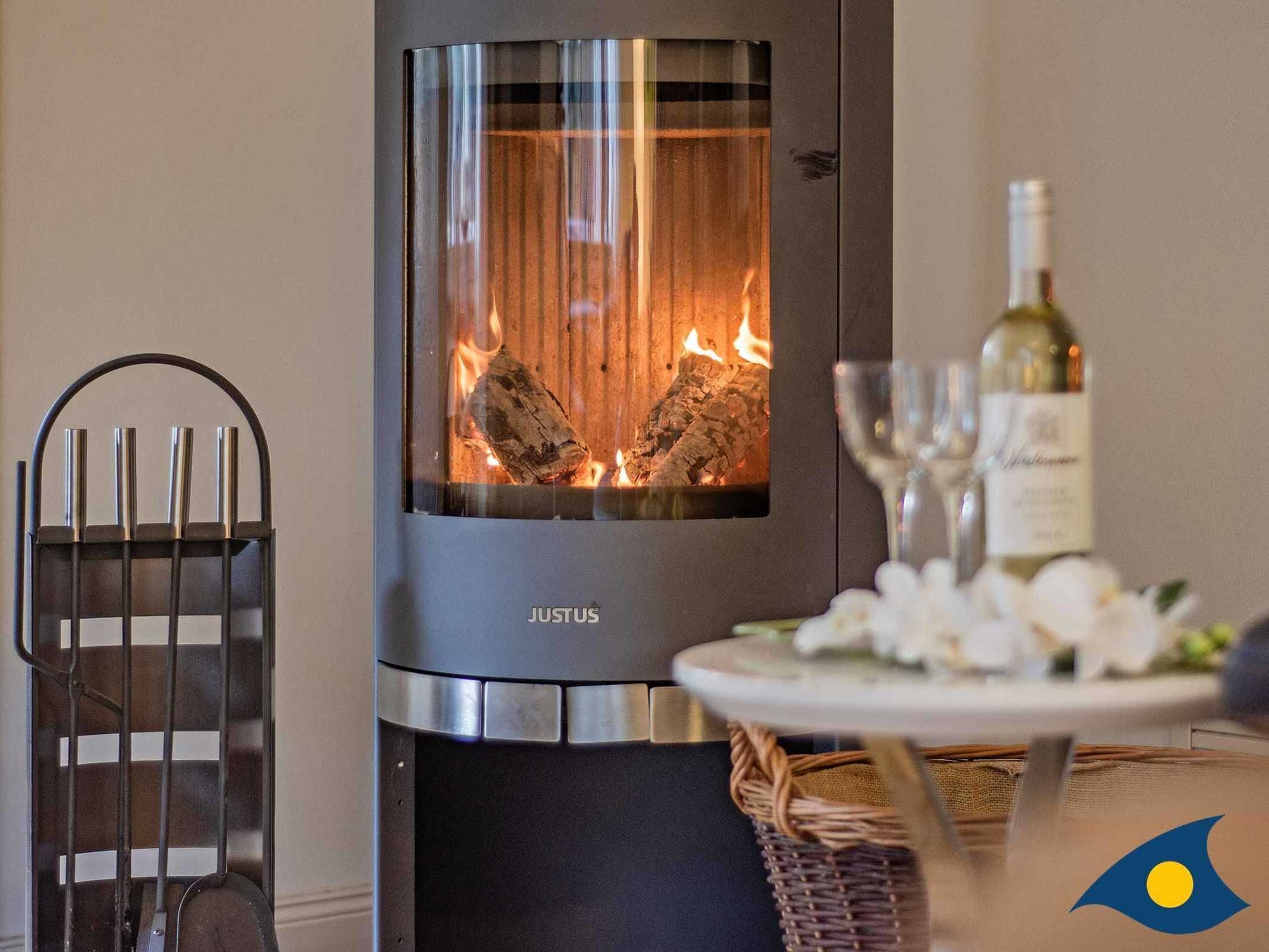 A modern fireplace with a glass front, a metal chair, a bottle of wine, and a glass on a table.