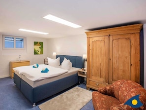 Um quarto com cama, mesas de cabeceira, guarda-roupa e uma cadeira.