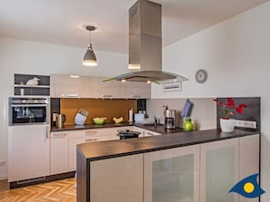 Uma cozinha moderna com ilha central, forno embutido e eletrodomésticos de aço inoxidável.