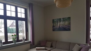 A living room with a sectional sofa, a wooden coffee table, and a painting of a forest on the wall. - Fewo Moltke Villa - Moltke Villa (Teterow)