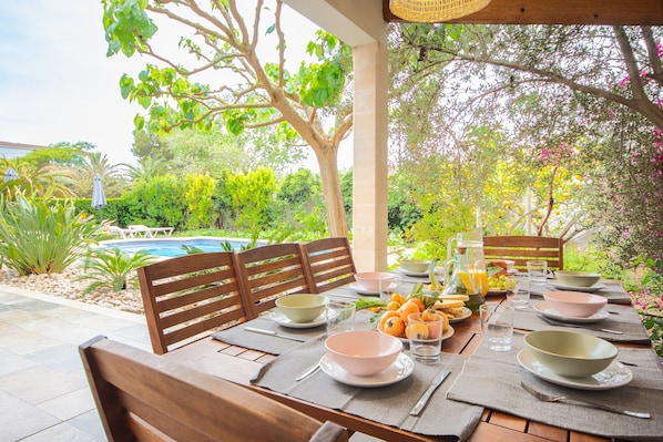 An outdoor dining area with a pool, wooden chairs, and a table set with bowls and glasses.