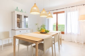 A dining area with a wooden table, white chairs, a cabinet with glass doors, and hanging wicker pendant lights.