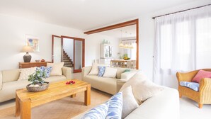 Una sala de estar con un sofá, una mesa de centro, una silla de mimbre y un comedor al fondo.