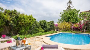Una piscina con sillones de descanso, una botella de champán y una mesa con flores.