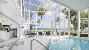 Un espace piscine intérieure avec vue sur l’océan, une cuisine et un coin salon extérieur.