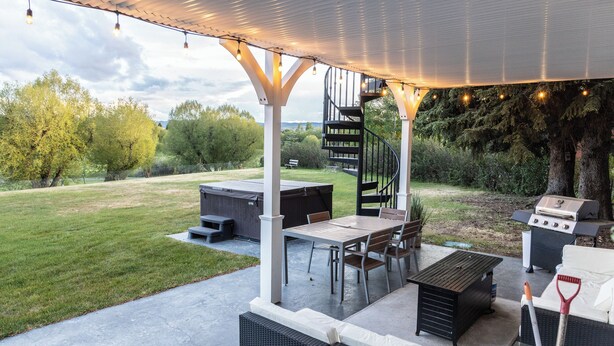 Eine Terrasse im Freien mit überdachter Sitzgelegenheit, einem Grill und einer Wendeltreppe.