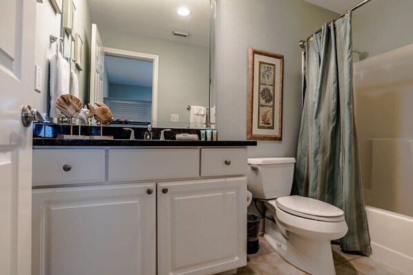 Un baño con inodoro blanco, lavamanos con encimera negra y cortina de ducha.