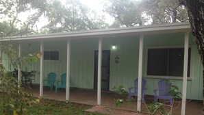 A covered porch with green walls and white columns, featuring two chairs and a small table.