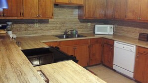 A kitchen with wooden cabinets, a granite countertop, a sink, a microwave, and a dishwasher.