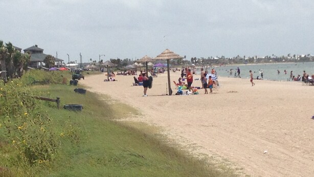 A beach with people, umbrellas, and beach huts.