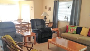 A living room with a sofa, armchairs, a coffee table, and a dining area with chairs and a table.
