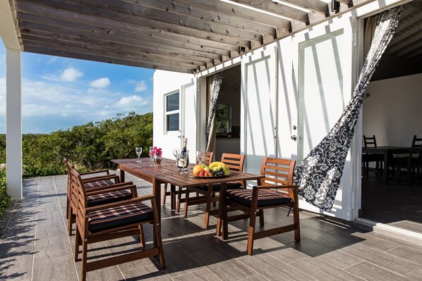 An outdoor dining area with a wooden table and chairs, a bottle of champagne, and a fruit bowl.
