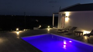 Ein moderner Poolbereich im Freien mit einem blau beleuchteten Pool, Liegestühlen und stimmungsvoller Beleuchtung.