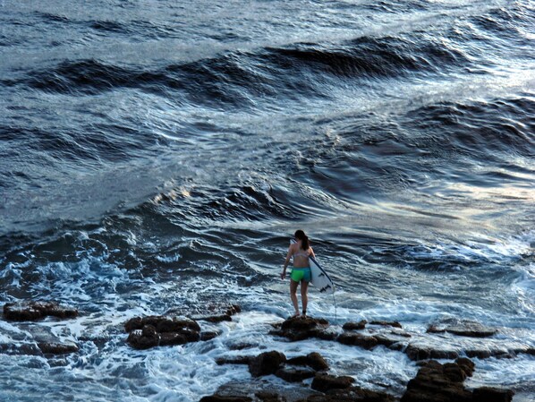 Una persona de pie sobre rocas junto al océano con una tabla de surf.