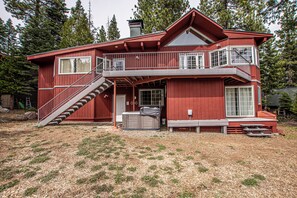 Une maison rouge en bois à deux étages, dotée d’un balcon, d’un escalier et d’un espace extérieur aménagé et abrité.