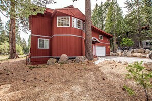 Une maison rouge à deux étages, avec un garage, entourée d’arbres et de rochers.