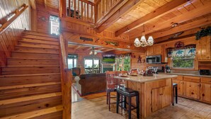 A wooden cabin interior with a staircase, kitchen, and dining area.