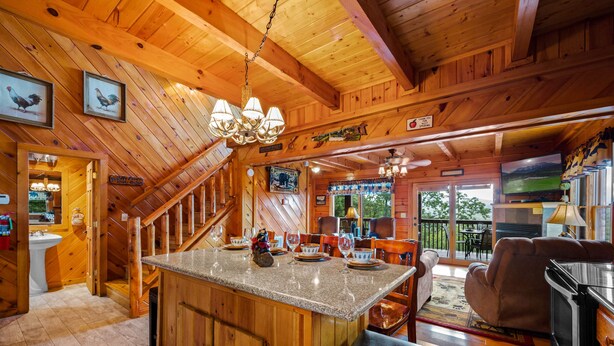 A wooden cabin interior with a kitchen island, dining area, and a staircase leading to an upper level.