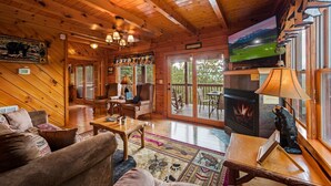A cozy cabin interior with wooden walls, a fireplace, a television, and a dining area.