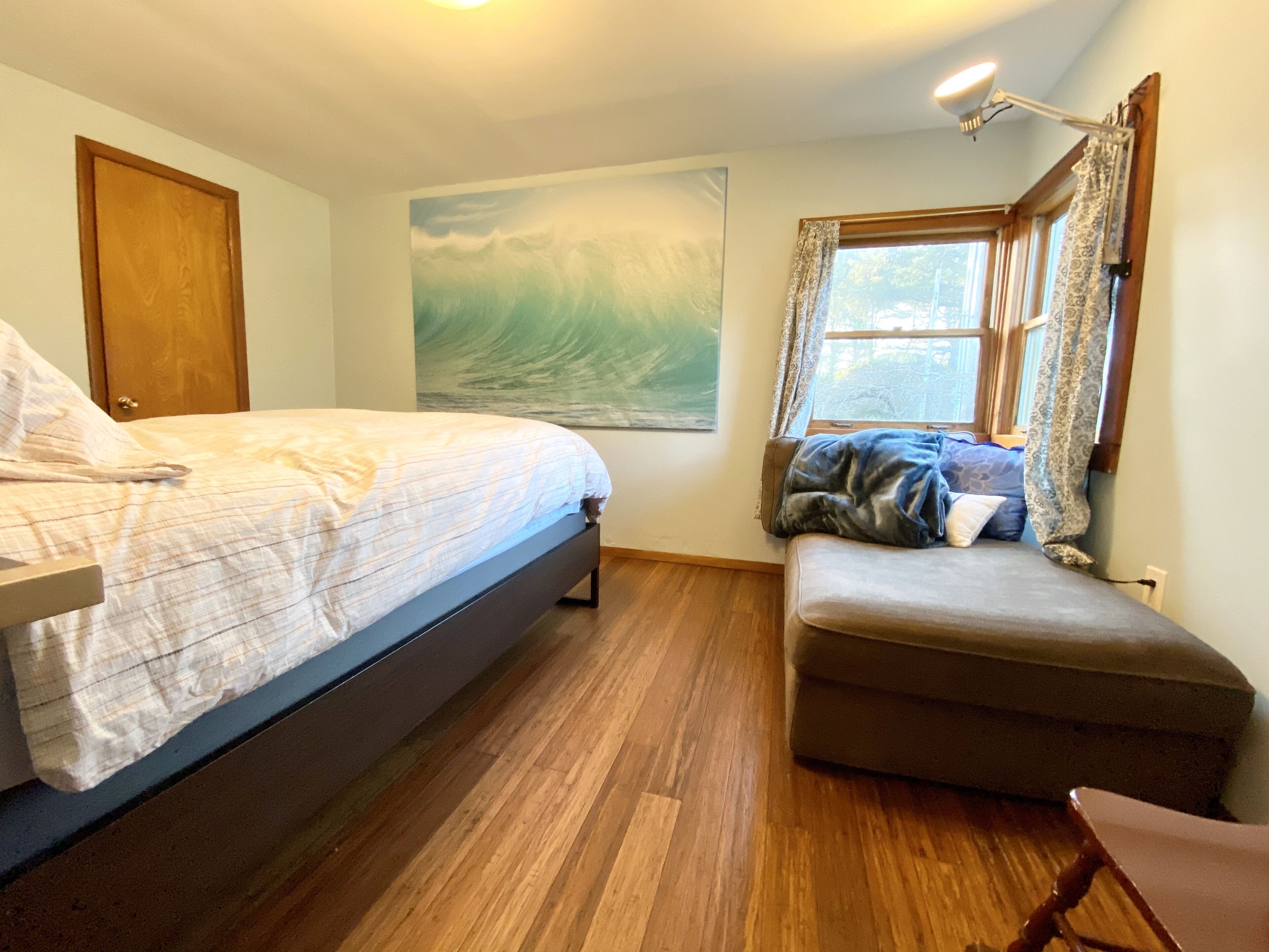 A bedroom with a bed, a bench, a painting, and a window with curtains.