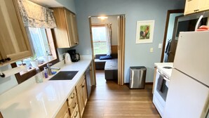 A narrow kitchen with wooden cabinets, a white refrigerator, and a window with a curtain.