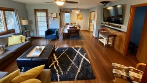 A spacious living room with a sofa, a coffee table, and a TV. There is a dining area with a table and chairs.