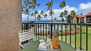 Een balkon met een eettafel gedekt voor twee personen, met uitzicht op een zwembad en resort, palmbomen en de oceaan.