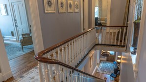 A staircase with white balusters and a wooden handrail, leading to a second-floor area with a patterned rug and a seating area.