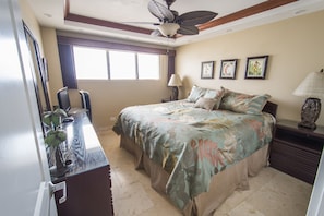 Relax in this inviting space with a large bed, desk, and chair, surrounded by artwork and a plant.