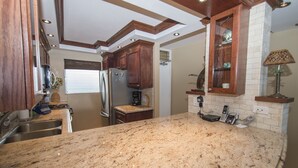A kitchen with granite countertops, wooden cabinets, a stainless steel refrigerator, and a built-in oven. - Spectacular! Full A/C Penthouse Level Ocean Front 1 Bedroom - # 608 (Kihei)
