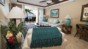 A living room with a ceiling fan, a sofa, a coffee table, and a view of the outdoors. - Spectacular! Full A/C Penthouse Level Ocean Front 1 Bedroom - # 608 (Kihei)