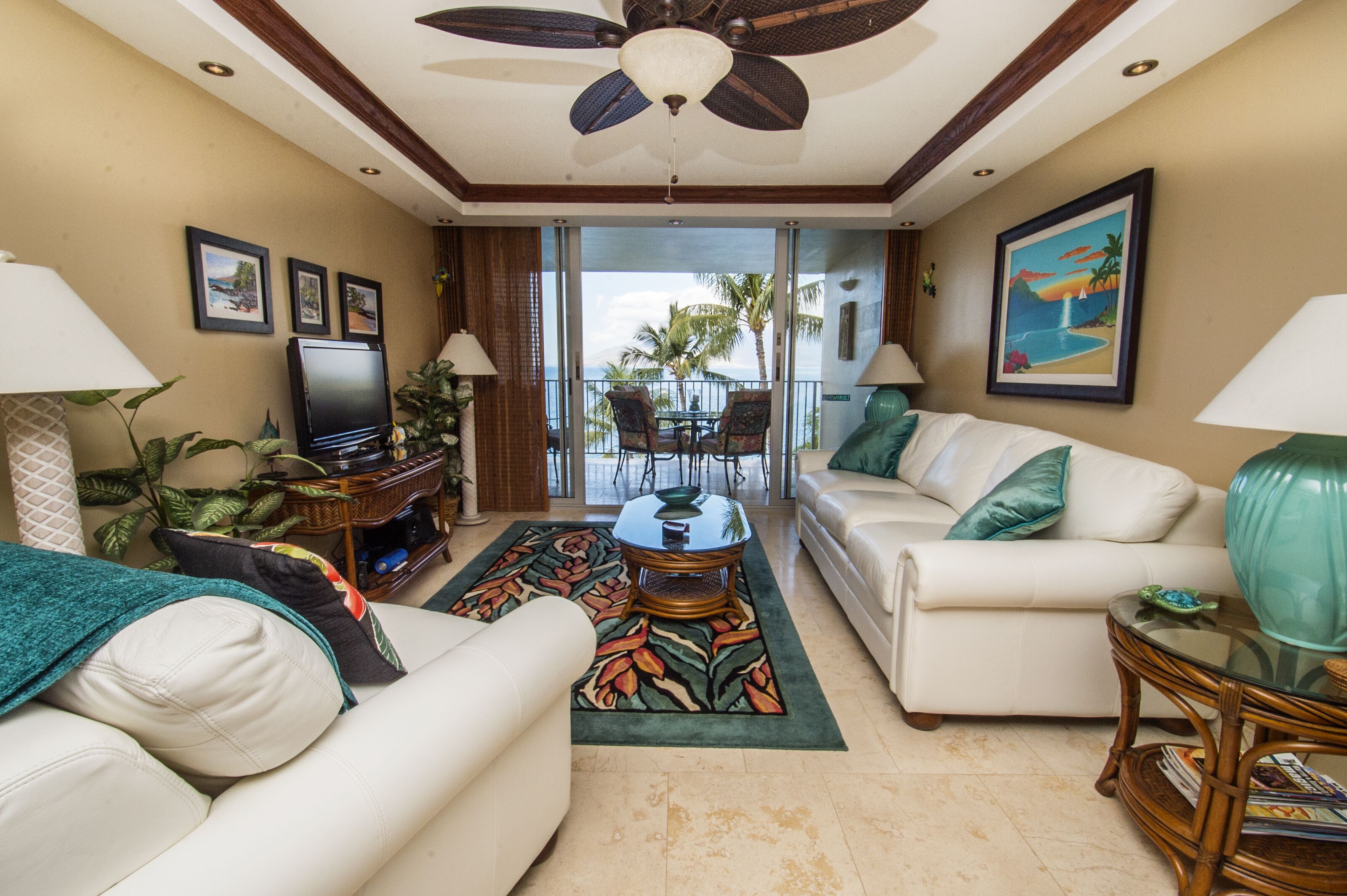 A living room with a ceiling fan, a television, a sofa, a coffee table, and a view of the outdoors.