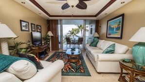 A living room with a ceiling fan, a television, a sofa, a coffee table, and a view of the outdoors. - Spectacular! Full A/C Penthouse Level Ocean Front 1 Bedroom - # 608 (Kihei)