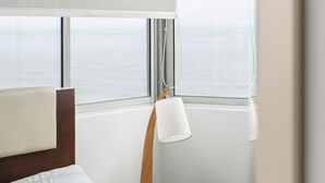 Habitació d'hotel amb llit, taulell, làmpada i finestra amb persianes.