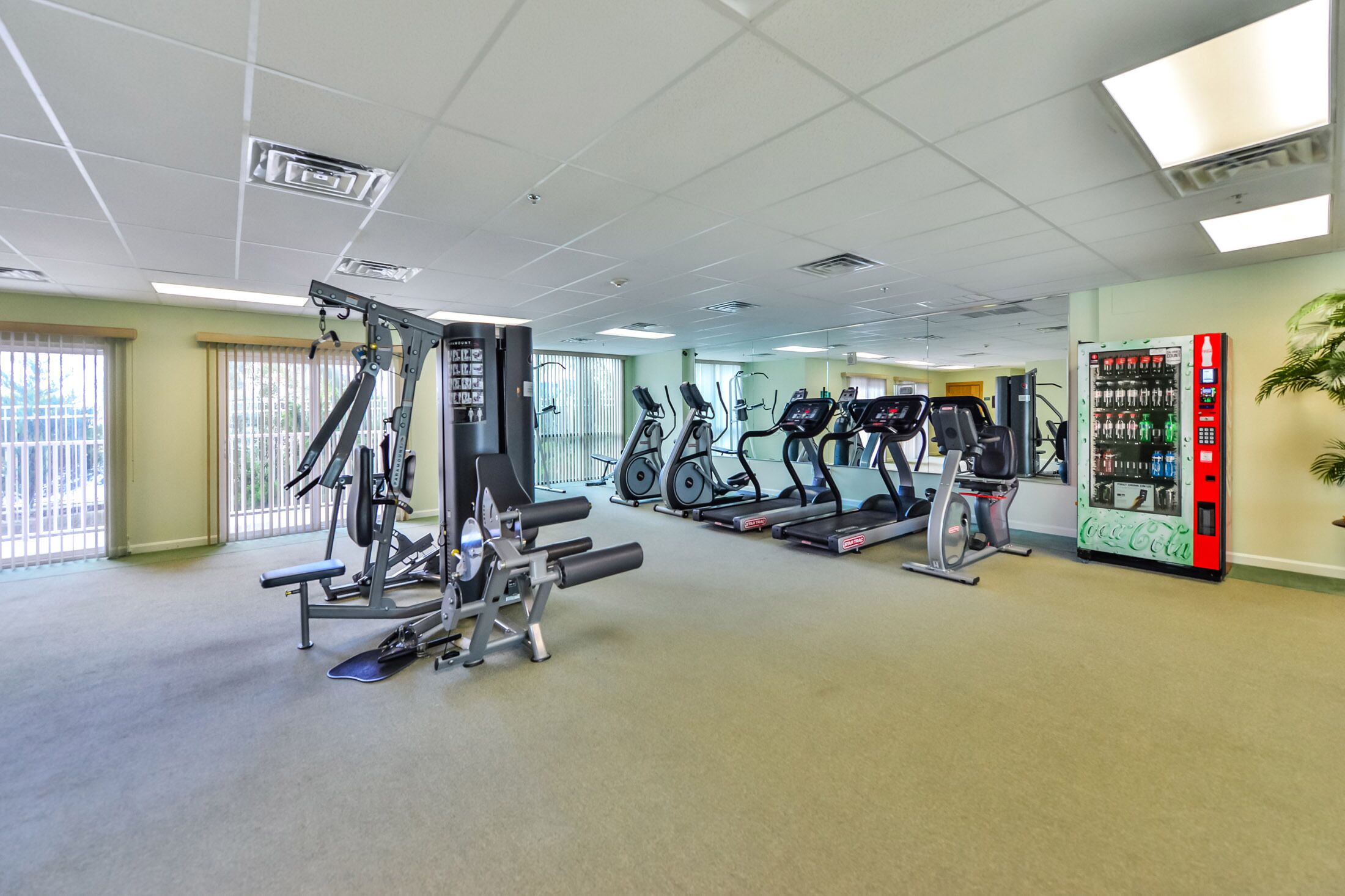 Une salle de sport équipée de divers appareils d’exercice, notamment des tapis de course et des appareils de musculation, ainsi qu’un distributeur automatique.