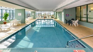 En indendørs swimmingpool med glasvægge, hvide stole og et skilt med 'NO DIVING'.