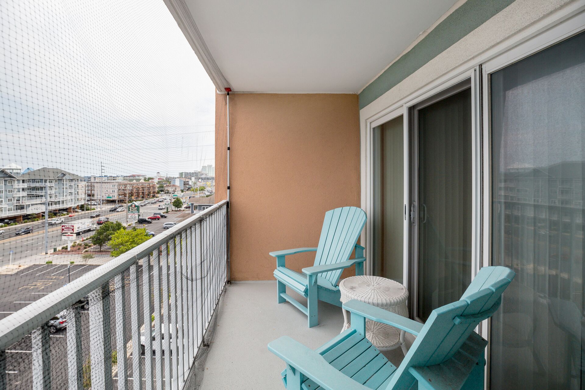 Un balcon avec deux fauteuils Adirondack bleu clair, une petite table ronde et une vue sur une rue de la ville, avec des immeubles et une enseigne d’hôtel.