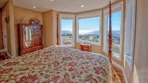 A bedroom with a large floral bedspread, a wooden dresser with a mirror, and a view of the ocean through large windows. - Luxury, Full Views, 6 Bedrooms/5 Full Baths, 3,800+ s.f., Pool Table, Hot Tub (Bodega Bay)