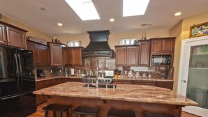 A kitchen with dark wood cabinets, a large island with bar stools, a black refrigerator, and a microwave. - Luxury, Full Views, 6 Bedrooms/5 Full Baths, 3,800+ s.f., Pool Table, Hot Tub (Bodega Bay)