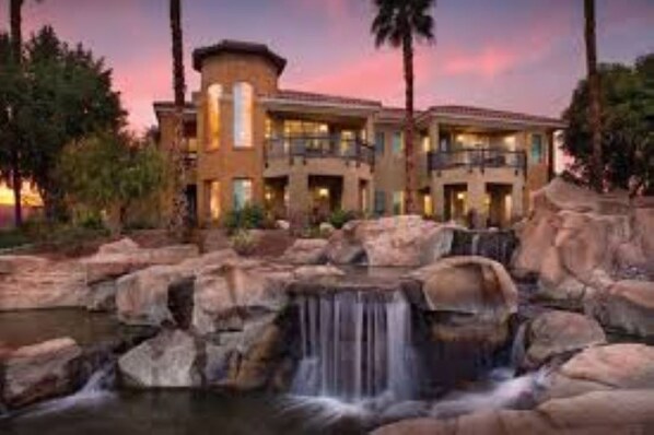 Guests can enjoy a serene atmosphere with a waterfall feature and pool, surrounded by lush greenery and palm trees.