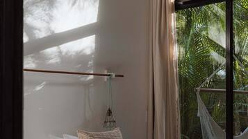 A bedroom with a bed, a hammock, and a view of palm trees through a window.