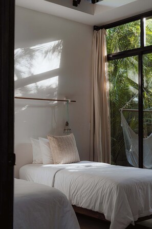 Een slaapkamer met een bed, een hangmat en uitzicht op palmbomen door een raam.