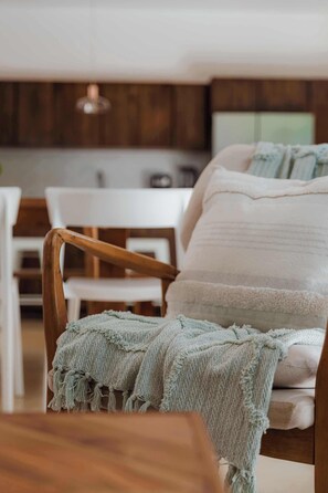 Een houten stoel met een groene gebreide plaid, een wit kussen en een houten tafel in een moderne keuken.