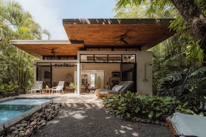 Une maison moderne dotée d’une piscine, de chaises longues et d’un ventilateur de plafond.
