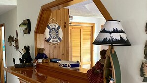 Een houten bar met een spiegel, een reddingsboei en een lamp. Drie krukken en een visdecoratie aan de muur.
