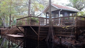 Een houten chalet met een veranda en een trap naar een terras boven het water.