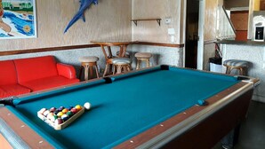 A pool table with a red sofa and chairs, a poster of a dolphin, and a kitchen area in the background. - In the HEART of Ocean Drive in North Myrtle Beach (North Myrtle Beach)