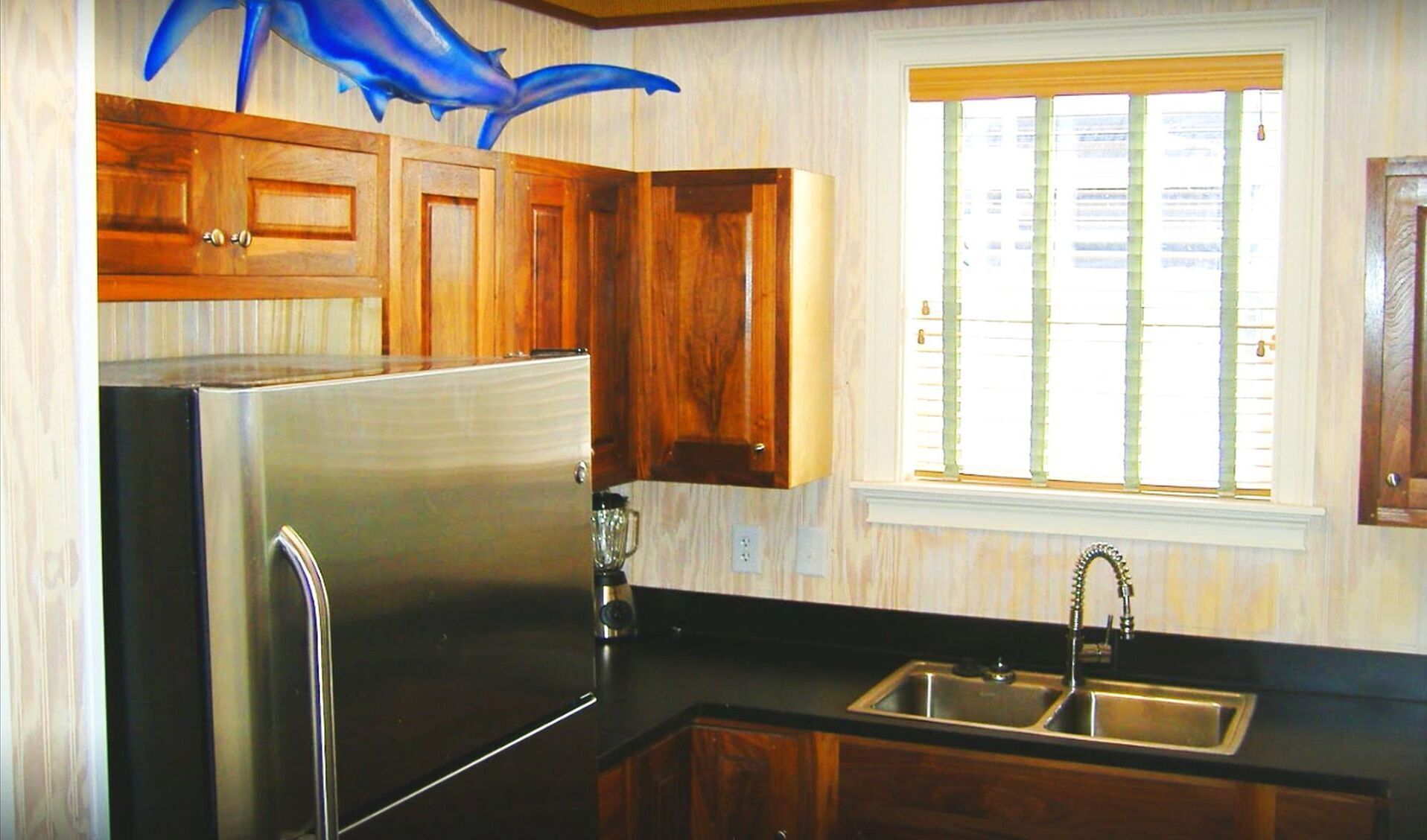 Eine Küche mit Holzausstattung, einem Edelstahlkühlschrank, einer Spüle und einem Fenster mit Jalousien.
