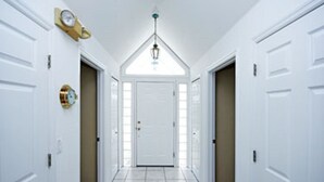 Ein Flur mit weißen Türen, einer Uhr an der linken Wand und einer Leuchte an der Decke.