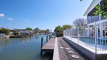 A waterfront property with a dock extending into a calm body of water, a white fence, and a building with a balcony.